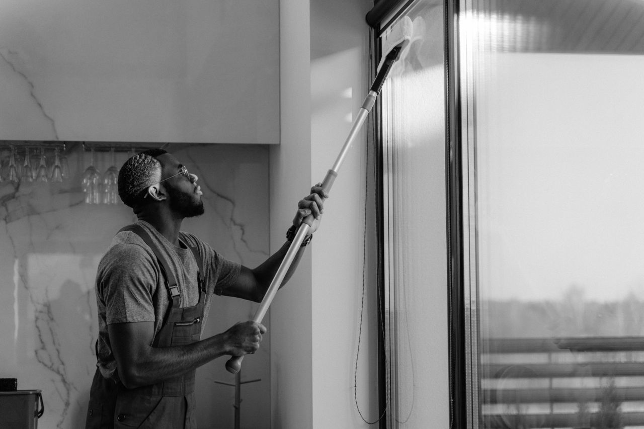services-01 A man cleaning a glass window with a mop in grayscale, showcasing professional work.